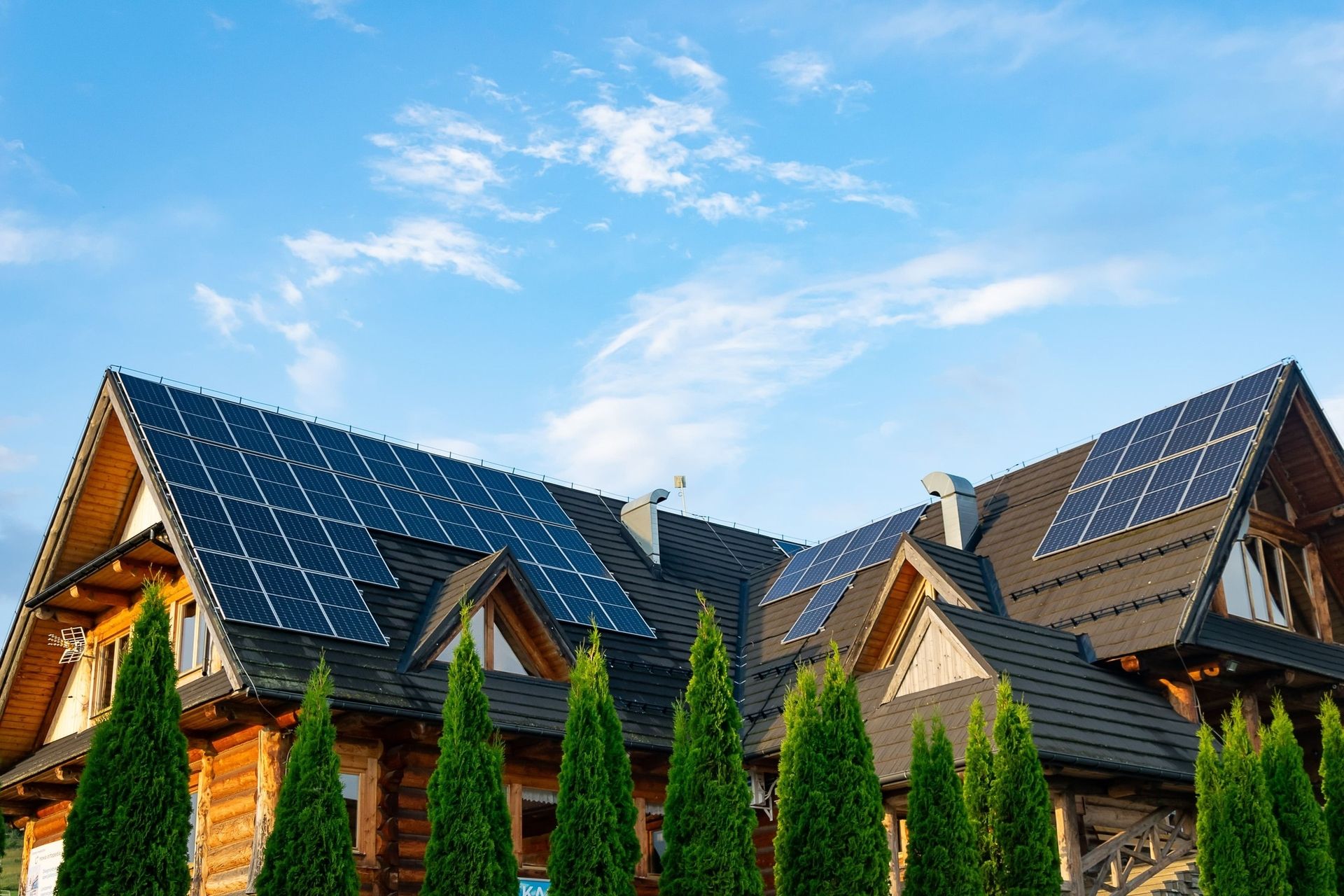 Ein Holzhaus mit schwarzem Dach und Photovoltaikplatten vor blauem Himmel